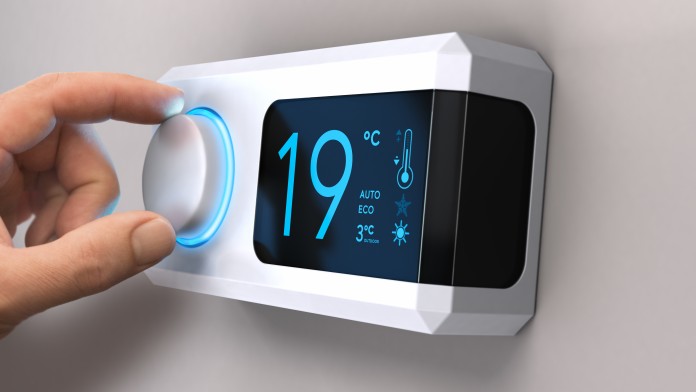 Hand turning a home thermostat knob to set temperature on energy saving mode. celcius units