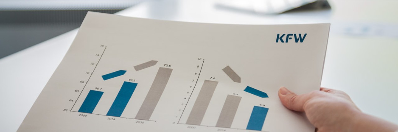 Eine Männerhand hält in einem Büro ein Papier mit Diagrammen