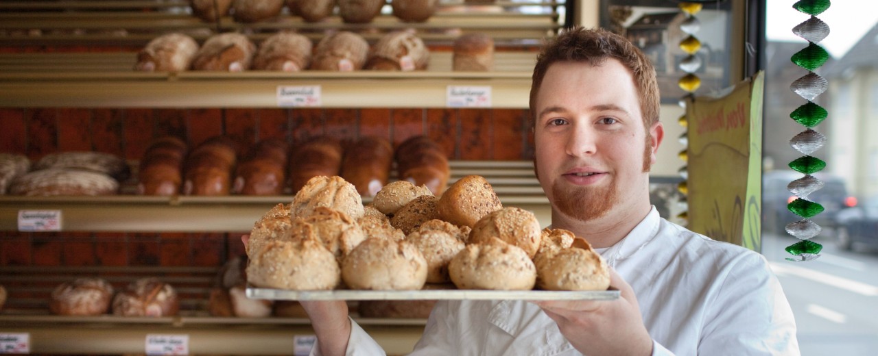 Ein Bäcker mit einem Bleck Brötchen in der Hand