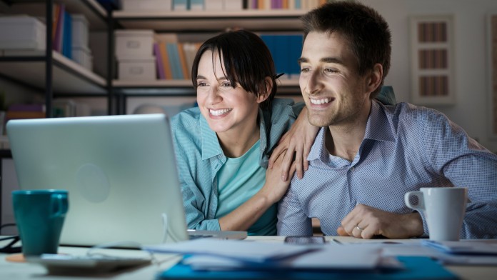 Happy smiling married couple at home using a laptop, connecting to internet and networking, communication and internet concept