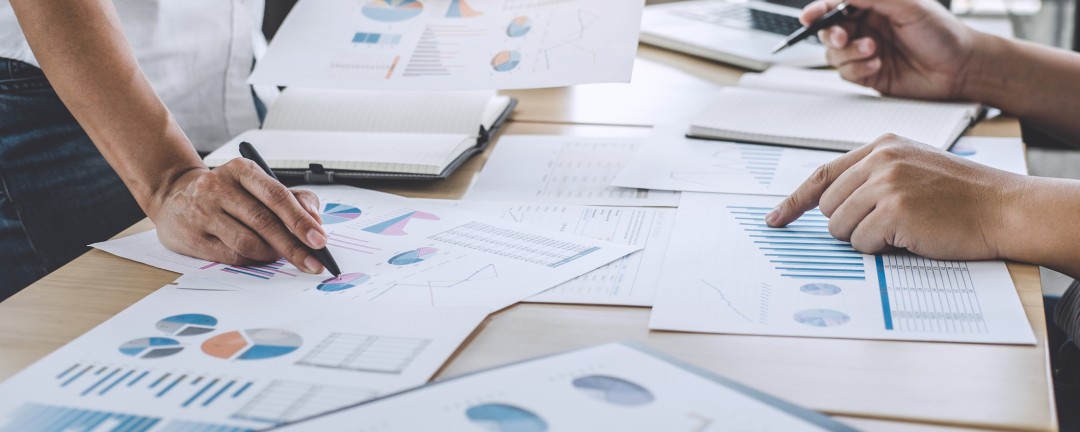 Viele Diagramme und Grafiken liegen auf dem Schreibtisch und werden besprochen