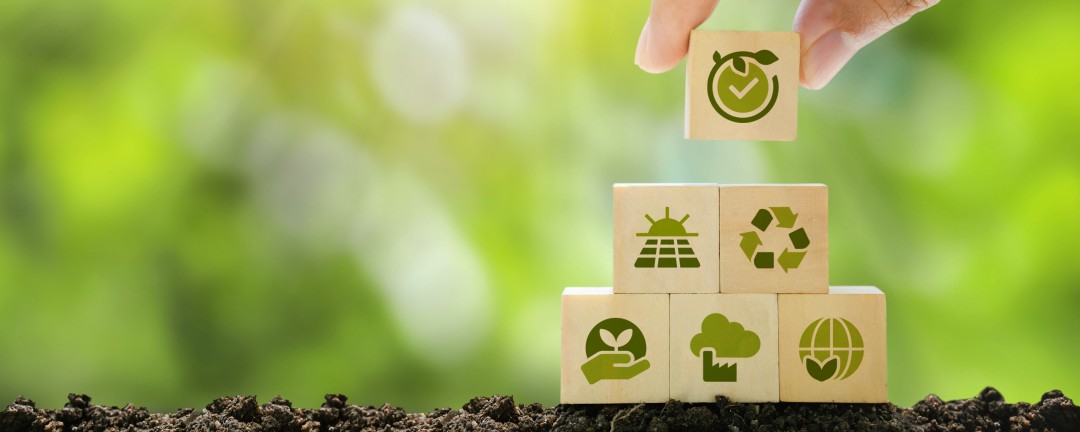Eine Hand stapelt Bauklötze mit Symbolen aus dem Klimaschutz drauf