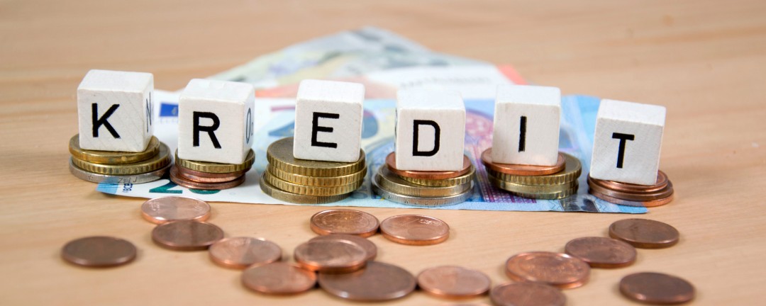 Auf Geldmünzen und Geldscheinen stehen Würfel mit der Aufschrift „Kredit“