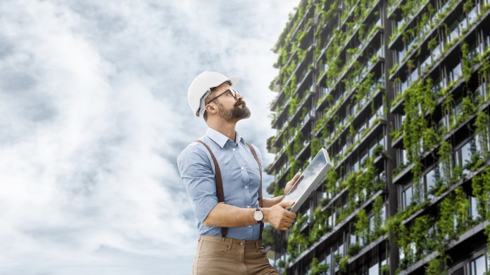 Man standing in front of a skyscraper overgrown with green plants