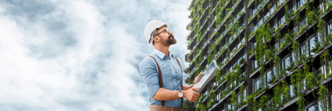  Man standing in front of a skyscraper overgrown with green plants 