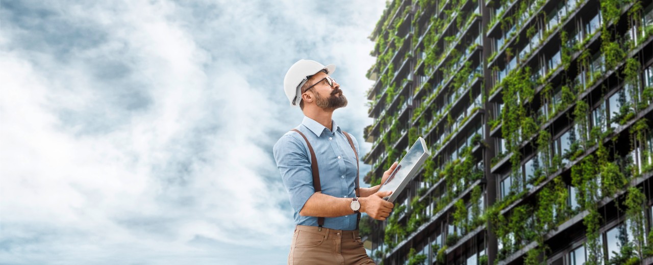 Man standing in front of a skyscraper overgrown with green plants