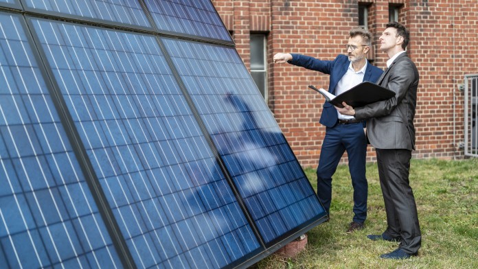 Two businessmen talking next to a solar panel in front of a brick building