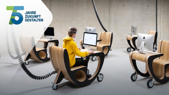 A woman sits in a modern classroom at a seat in front of a computer.