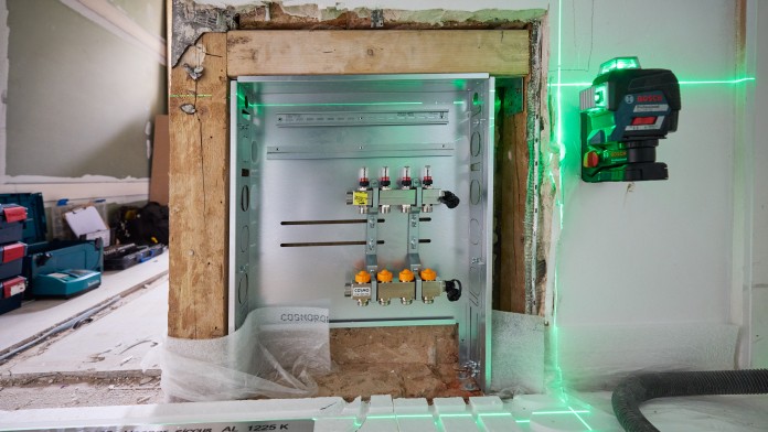 Offener Verteilerkasten in einer Wand mit grünen Laserlinien zur Ausrichtung und Messung. Baumaterialien im Vordergrund