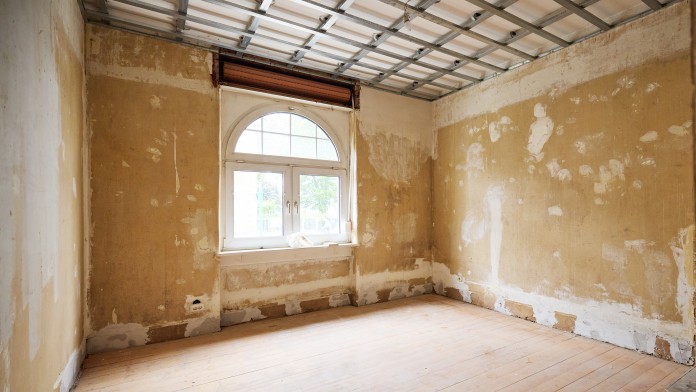 Leerer Raum mit abblätternden Wänden, Holzboden und einem Fenster mit Rundbogen im oberen Bereich
