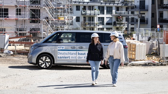 Zwei KfW Mitarbeiterinnen laufen vor einem parkenden VW Bus und einer Baustelle