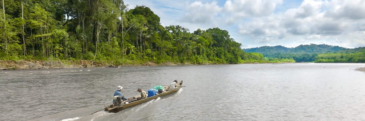 Drei Männer in einem kleinen Kanu auf einem Fluss neben dem Regenwald.