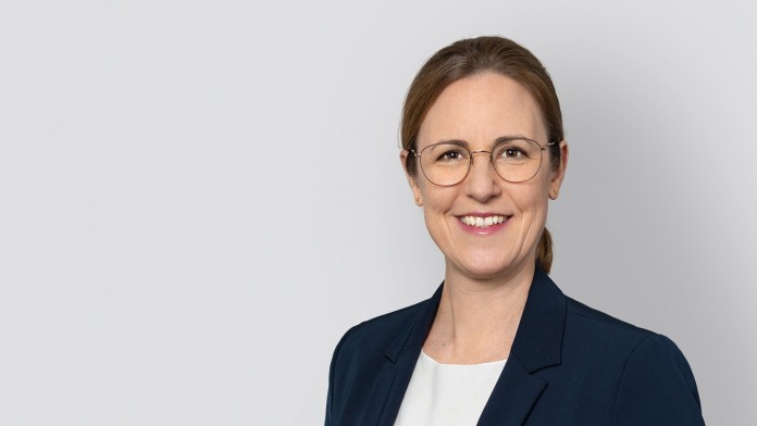 Portrait von Frau Berenike Wiener mit Brille, dunkelblauem Jackett und weißer Bluse vor hellgrauem Hintergrund
