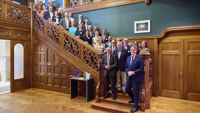 Eine größerer Gruppe Menschen posieren auf einer Holztreppe einer historischen Villa für ein Gruppenfoto