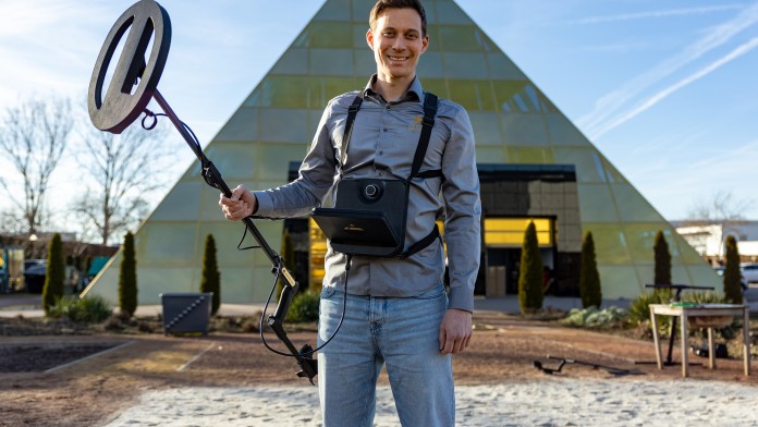 Ein OKM-Mitarbeiter hält vor dem OKM-Gebäude einen Metalldektor in der Hand