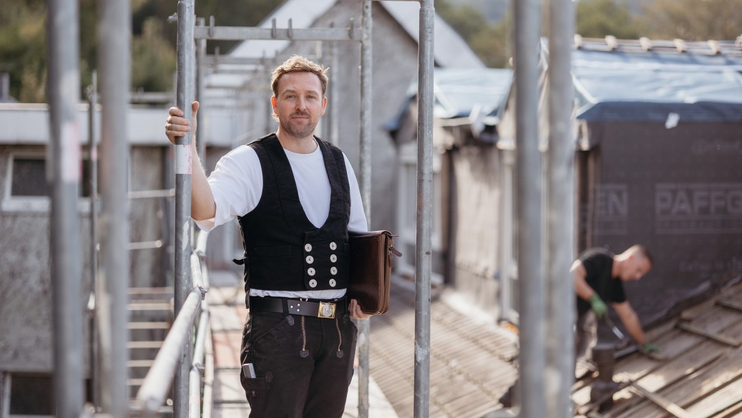 Dachdecker Felix Gutsche auf einem Baugerüst neben einem neugedeckten Dach