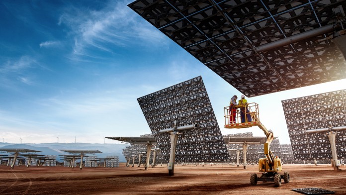 Zwei Personen auf einer Hebebühne vor großen, rechteckigen Solarpanelen mit Muster, die auf einem offenen Gelände aufgestellt sind