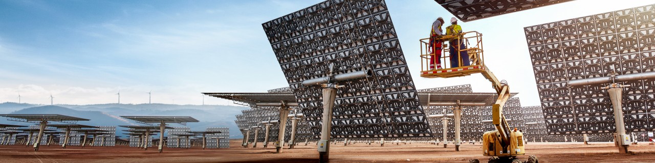 Zwei Personen auf einer Hebebühne vor großen, rechteckigen Solarpanelen mit Muster, die auf einem offenen Gelände aufgestellt sind