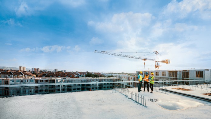 Mitarbeiter auf einer Baustelle, die Schutzausrüstung tragen und die nächste Bauphase besprechen – auf dem Bild sind Figuren in voller Größe zu sehen
