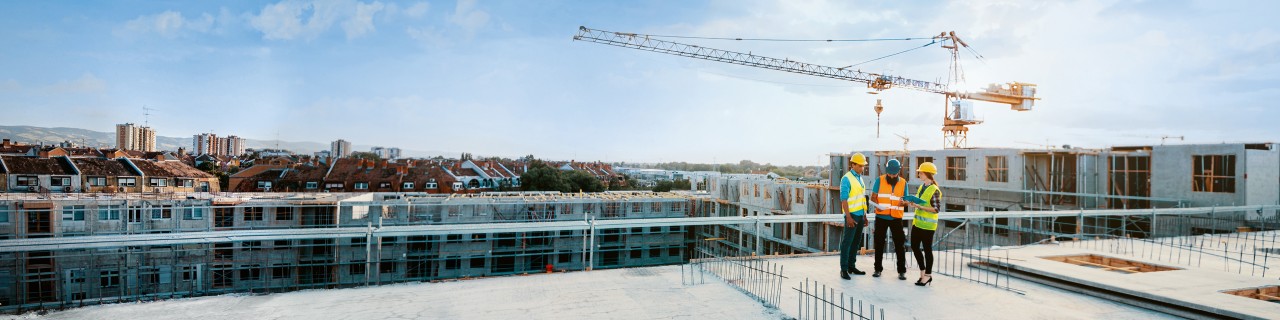 Mitarbeiter auf einer Baustelle, die Schutzausrüstung tragen und die nächste Bauphase besprechen – auf dem Bild sind Figuren in voller Größe zu sehen