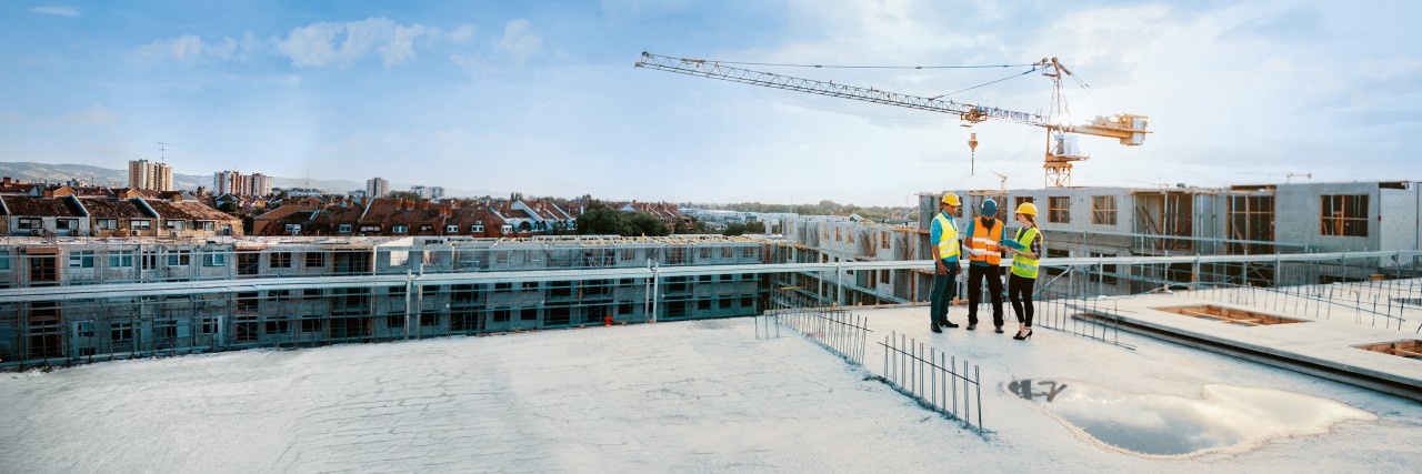 Mitarbeiter auf einer Baustelle, die Schutzausrüstung tragen und die nächste Bauphase besprechen – auf dem Bild sind Figuren in voller Größe zu sehen