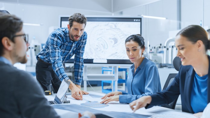 Vier Personen stehen und sitzen um einen Tisch herum