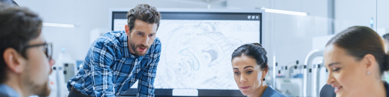 Vier Personen stehen und sitzen um einen Tisch herum