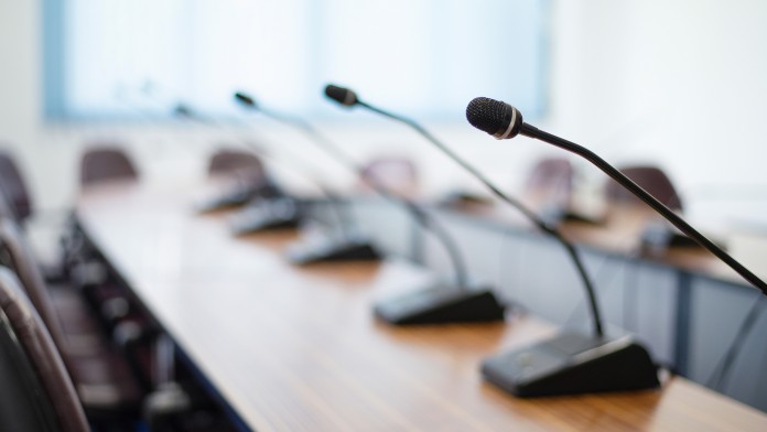A row of table microphones on a long conference table