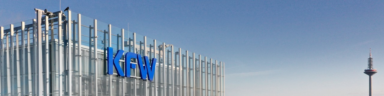 Drone shot of the KfW branch in Frankfurt. On the left is the main building with the KfW logo, on the right is a view of the Palmengarten, and in the distance is a television tower.