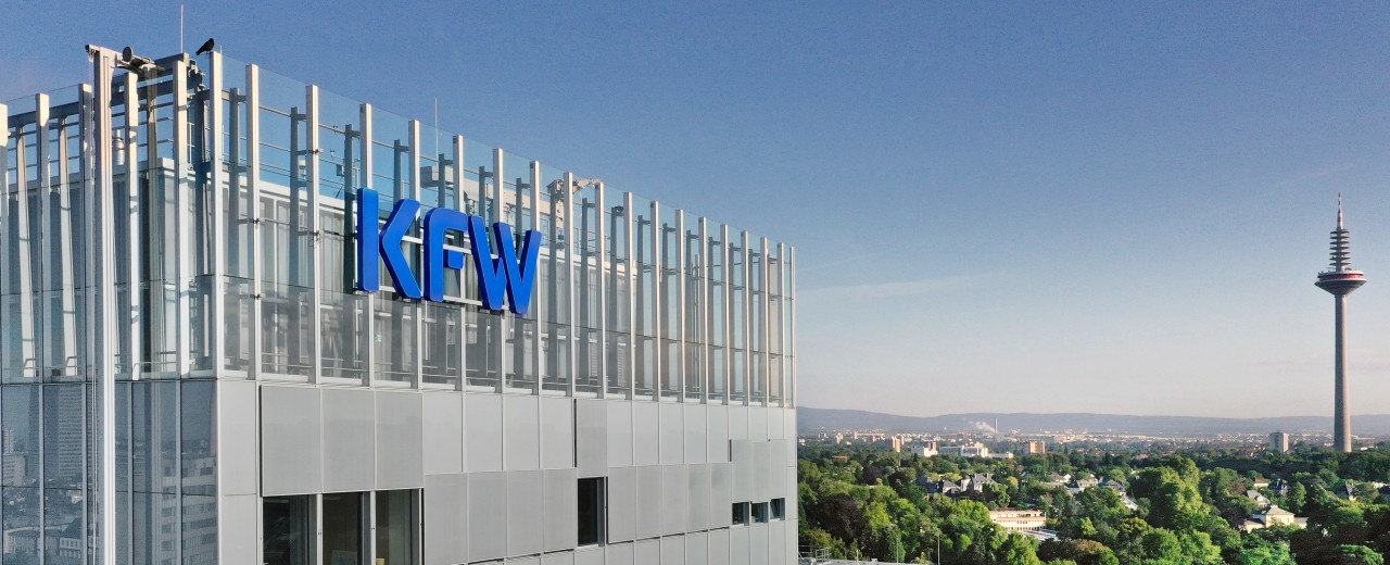 Drohnenaufnahme der KfW-Niederlassung Frankfurt. Links im Bild das Haupthaus mit KfW Logo, rechts Ausblick auf den Palmengarten und in der Ferne ein Fernsehturm.