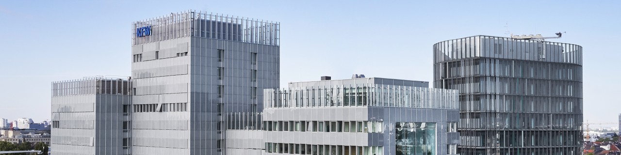 Drone image of the KfW building in Frankfurt. In the foreground, treetops from the Palmengarten, in the centre the KfW Main Building and IPEX, on the left in the background the Messeturm.