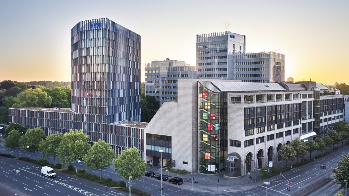 Drohnenaufnahme des KfW Gebäudes in Frankfurt bei Sonnenuntergang. Im Vordergrund eine Straßenkreuzung, links das IPEX Gebäude, rechtes die Nordarkade der KfW, im Hintergrund das Haupthaus der KfW.