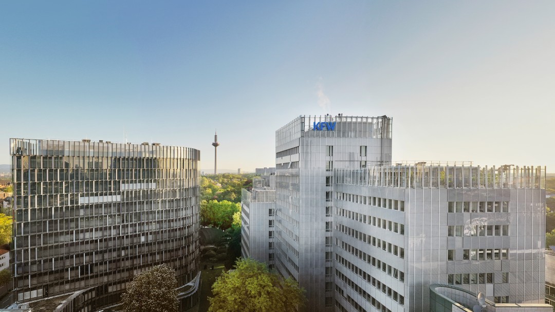 Drohnenaufnahme des KfW Standorts in Frankfurt. Im Vordergrund das Dach der Nordarkade, mittig im Bild das Gebäude der IPEX und das KfW Haupthaus. Der Himmel darüber ist wolkenlos.