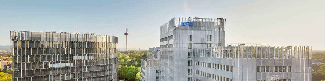 Drone recording of the KfW location in Frankfurt. In the foreground the roof of the northern arcade, in the middle of the picture the IPEX building and the KfW main building. The sky above is cloudless.