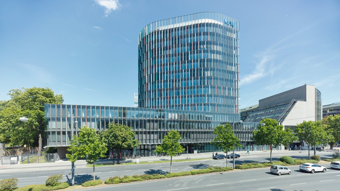 Blick auf das KfW IPEX-Gebäude in Frankfurt an der begrünten Hauptstraße. 