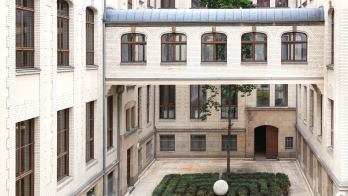 Green inner courtyard of the KfW building Berlin. A passageway connects both sides of the first floor.