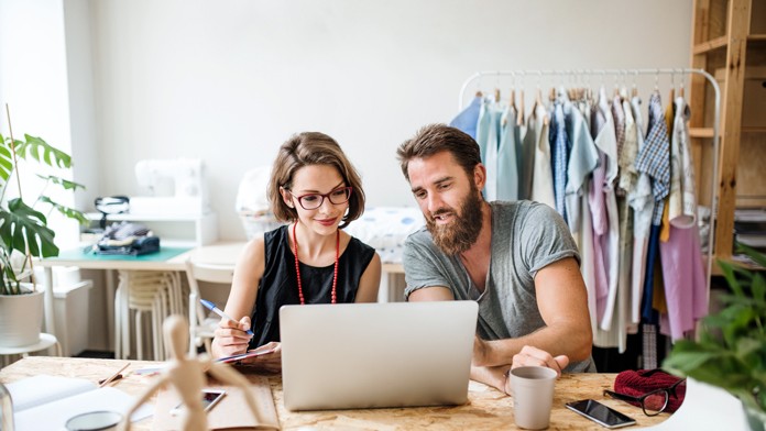 Eine Frau und ein Mann schauen in einem Atelier gemeinsam auf einen Laptop