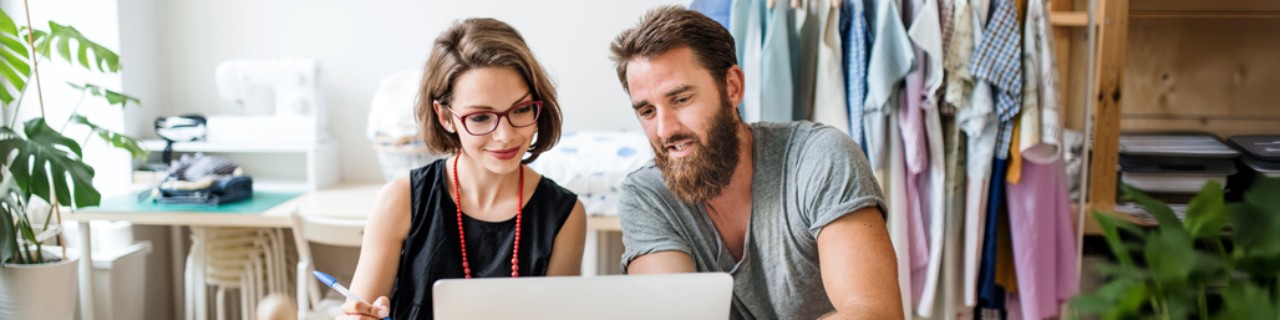 Eine Frau und ein Mann schauen in einem Atelier gemeinsam auf einen Laptop