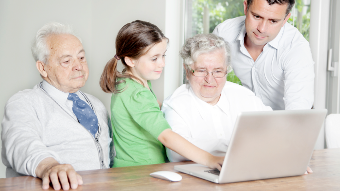 Zwei Senioren mit einem Kind und einem Mann mittleren Alters vor einem Laptop
