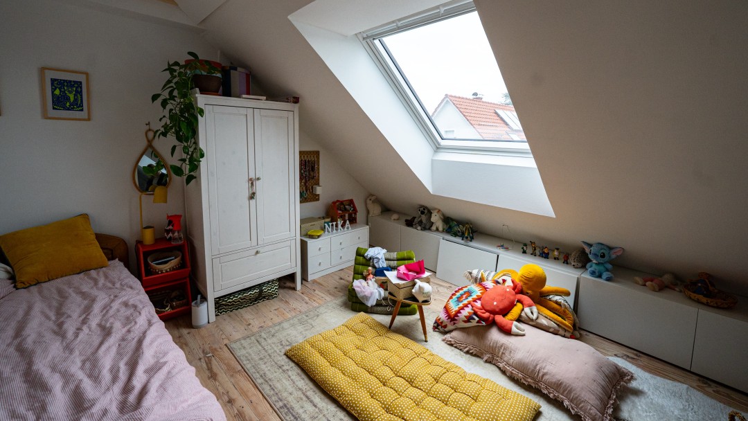 Kinderzimmer im Dachgeschoss mit Dachfenster, Schrank, Bett und Matratze und Spielzeug auf dem Boden