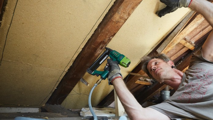 Eine Person liegt auf der Seite und befestigt die Dämmungspanele mit einem Tacker