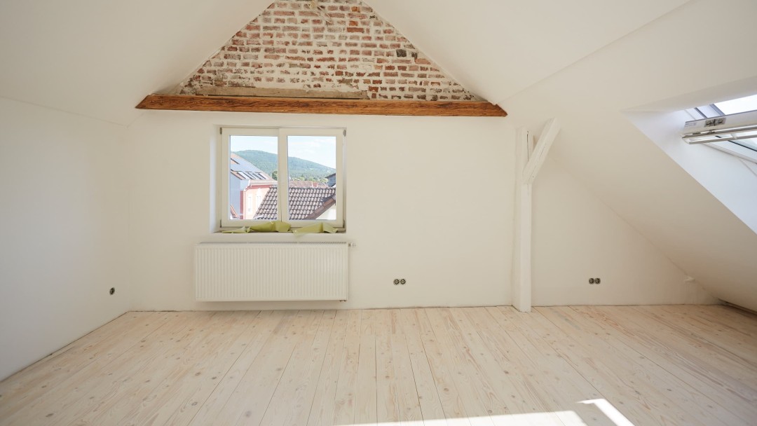 Blick in ein fertig saniertes Dachgeschoss mit einem seitlichen und einem Dachfenster, durch das die Sonne auf das Parkett scheint