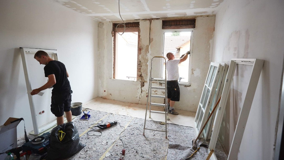 Zwei Personen stehen in einem Zimmer, das sich in Renovierung befindet und installieren zwei neue Fenster