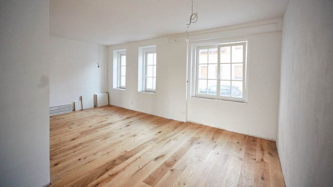 Blick in ein Zimmer mit drei Fenstern gegenüber, wo der Fußboden erneuert wurde