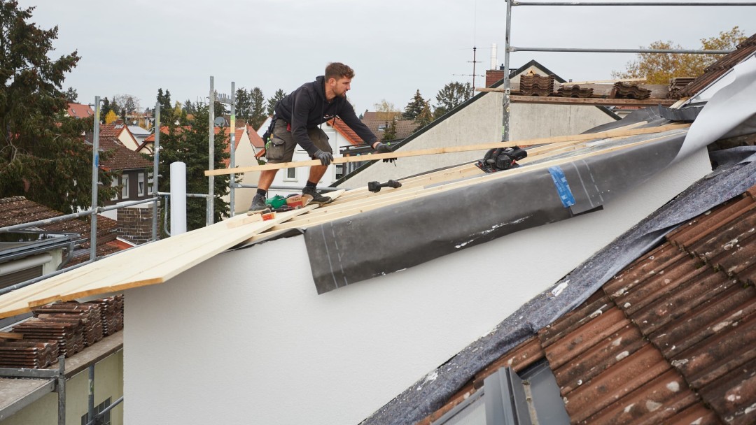 Eine Person steht auf einem Hausdach und deckt das Dach neu