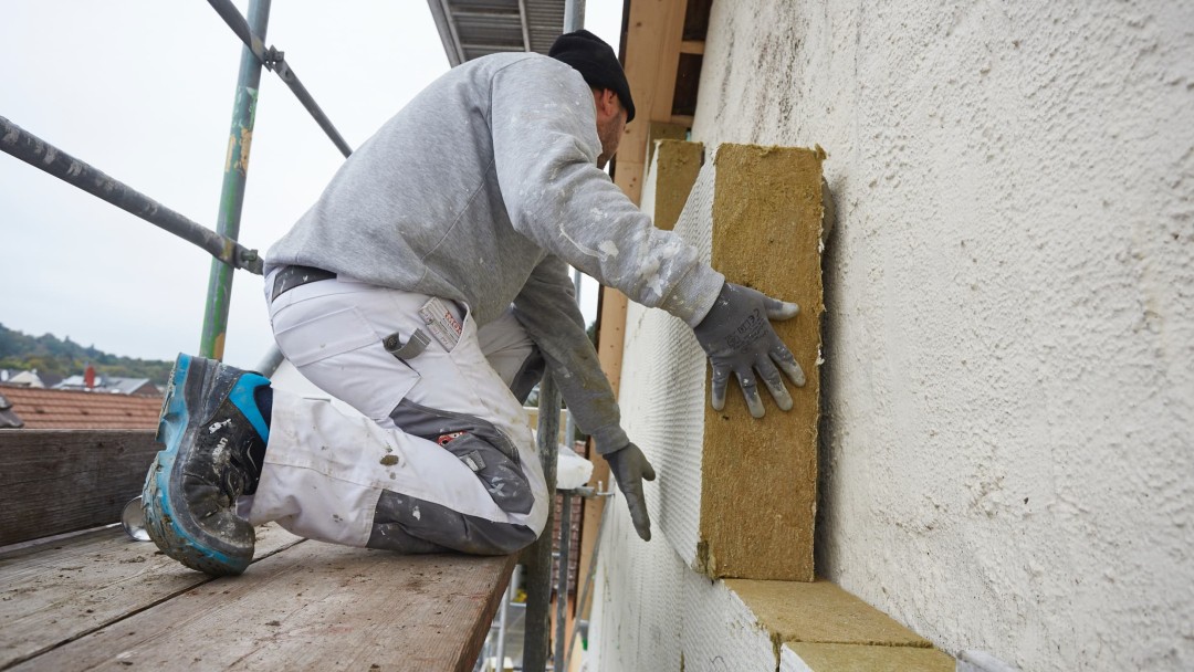 Eine Person arbeitet auf einem Gerüst, dämmt die Fassade eines Hauses
