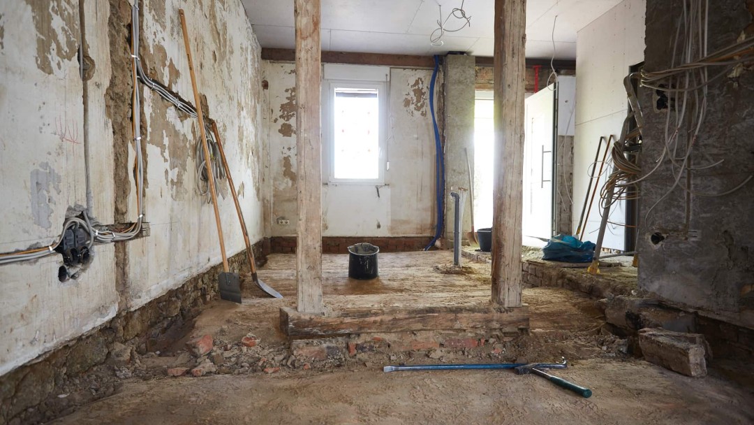 Blick in ein Haus im Rohbau, die Balken liegen frei, der Fußboden ist entfernt