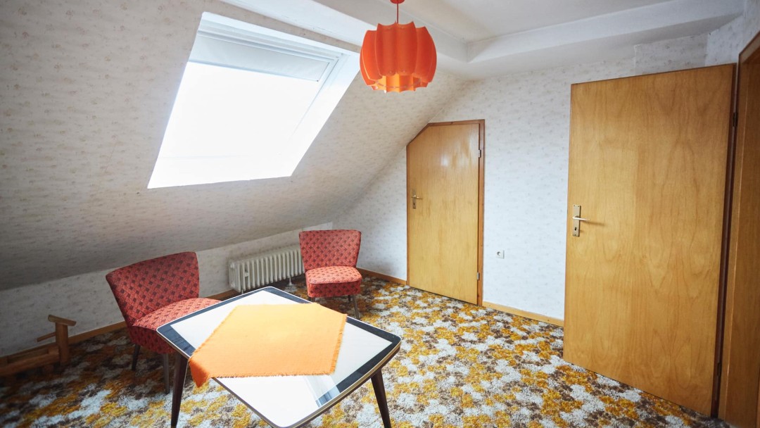 Blick in ein Zimmer vor der Sanierung mit alten Möbeln, Teppich und Türen