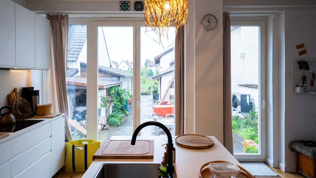 Blick in die Küche eines sanierten Hauses durch die bodentiefen Fenster auf die Terasse