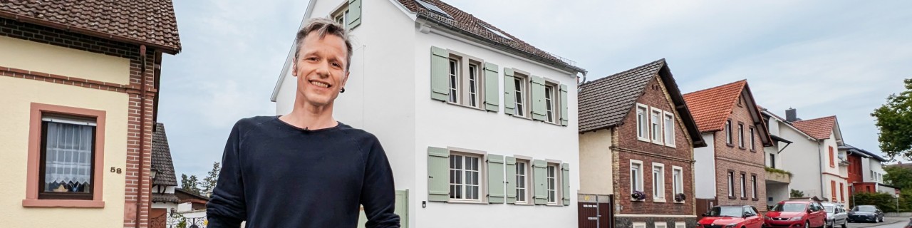 Der Sanierer steht auf der Straße vor seinem fertig sanierten Haus, das neben weiteren Häusern steht